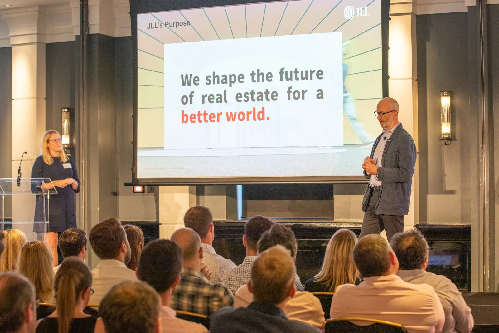 Two presenters on stage in front of the JLL Purpose slide at a corporate conference