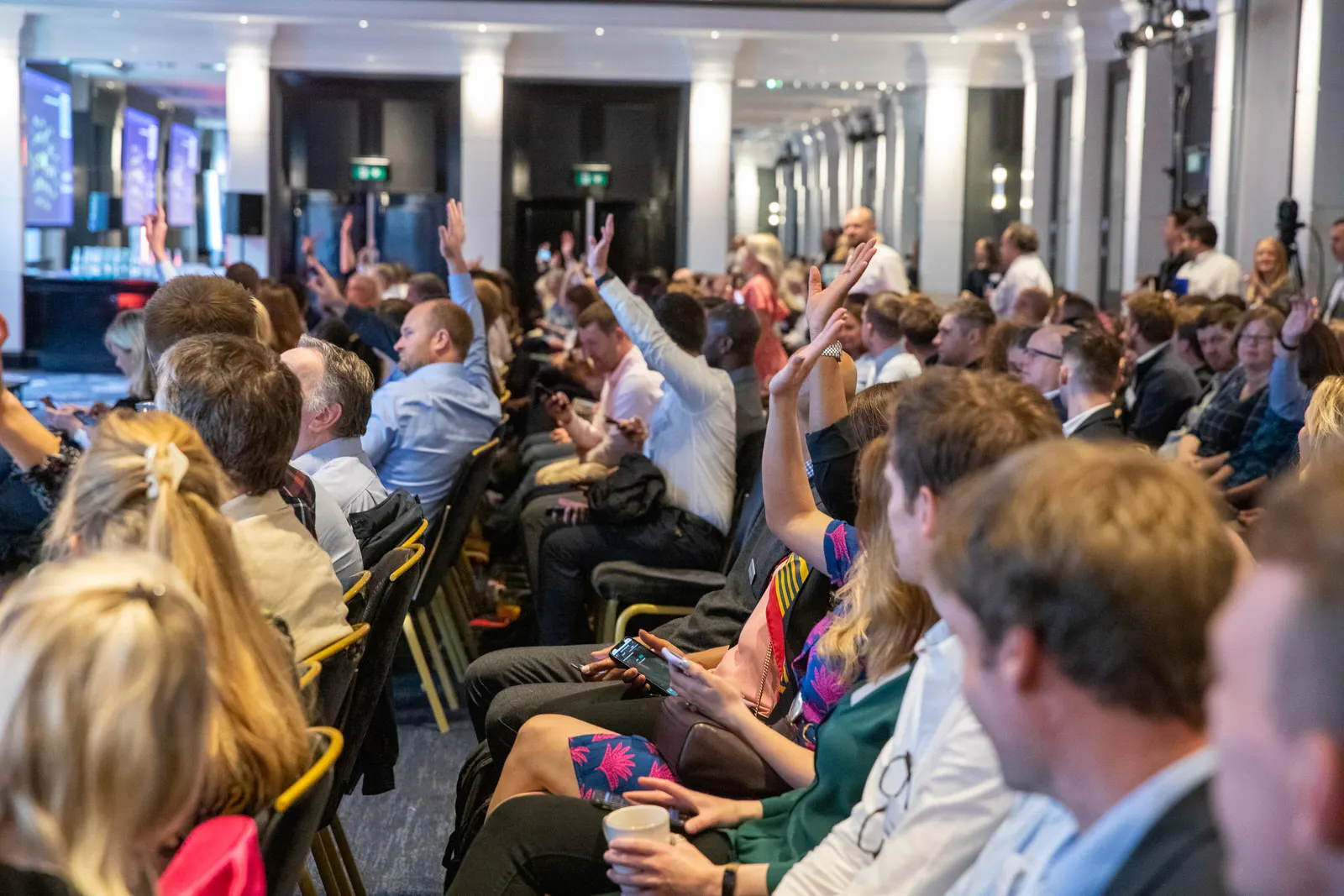 Conference delegates raising their hands during an interactive session in a grand ballroom