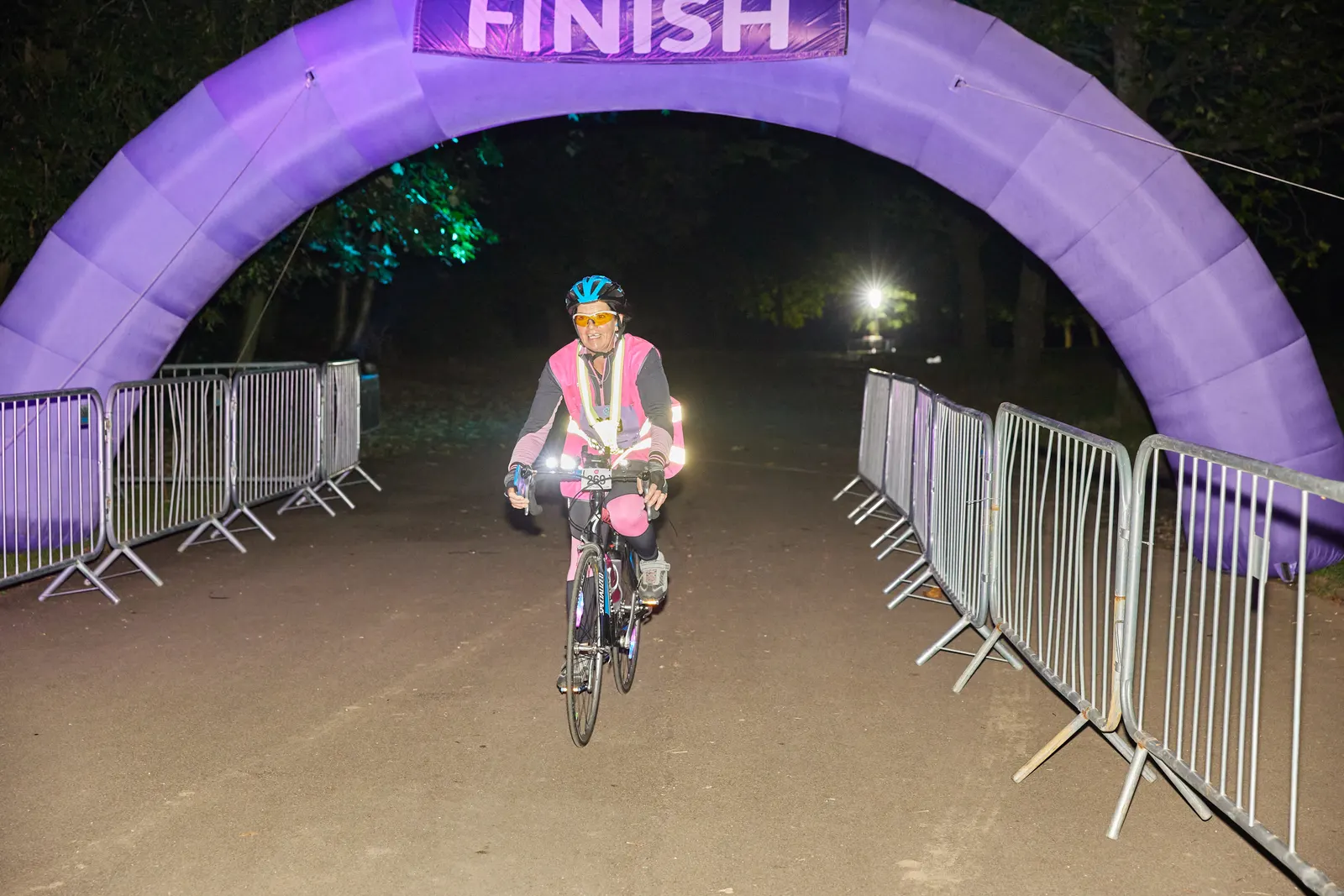 A cyclist crosses the illuminated finish arch at night in Heaton Park