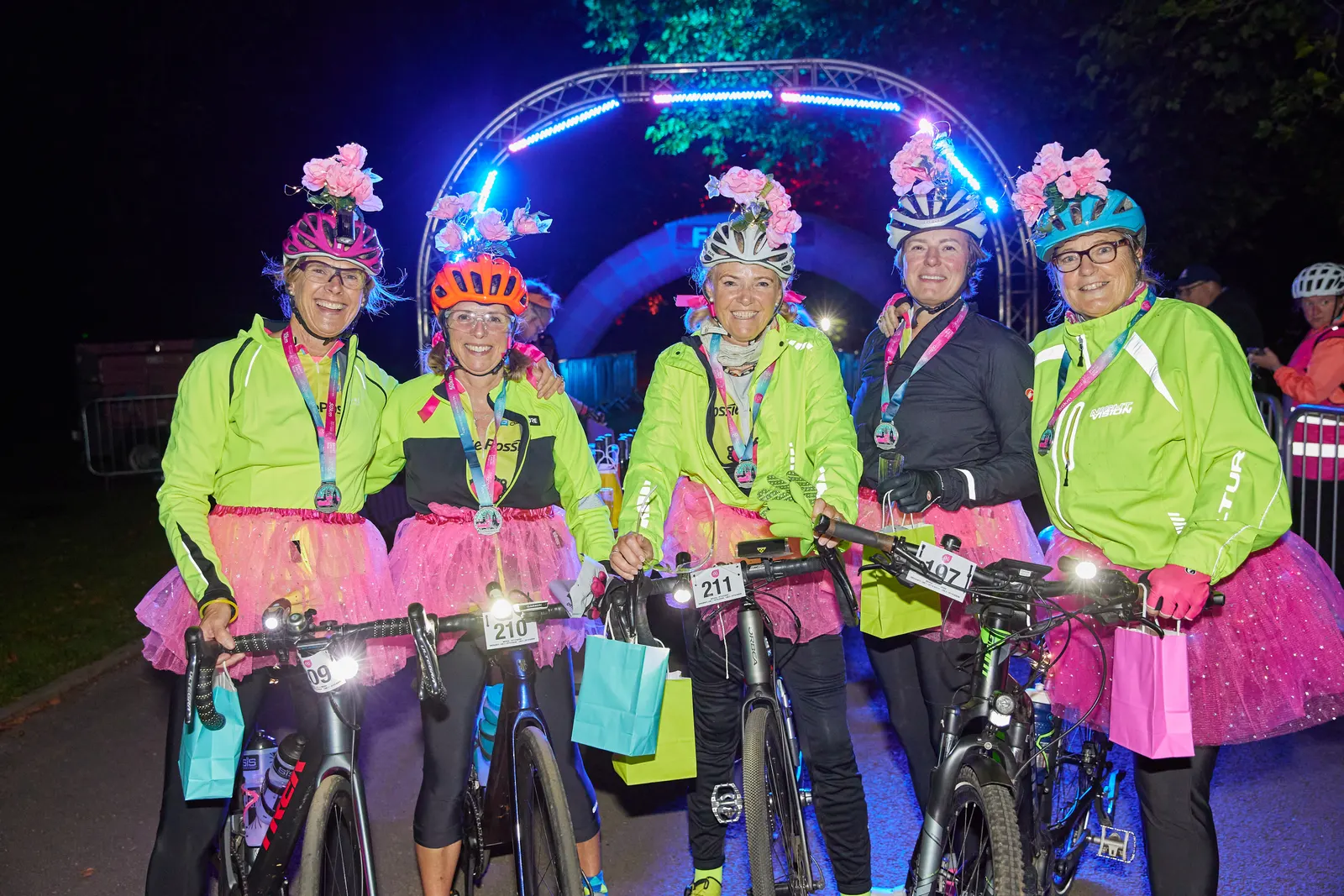 Group of riders celebrating with their medals at a night-time charity cycling event