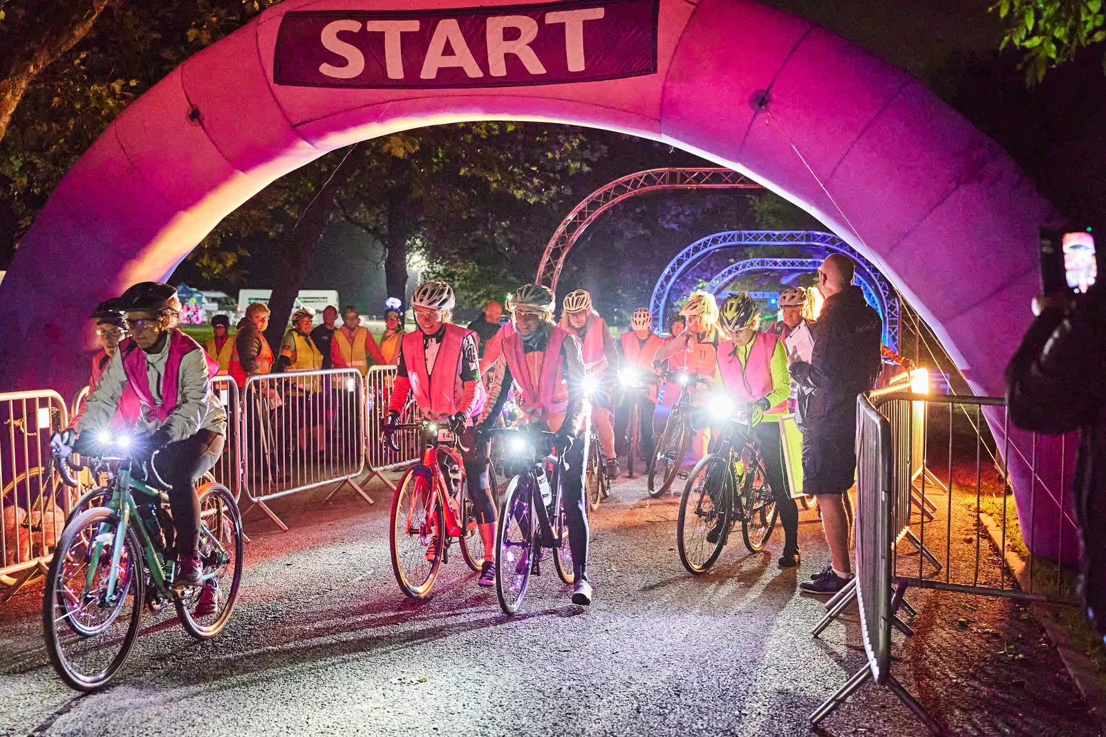 Riders stream under the start arch at an overnight charity ride in Heaton Park