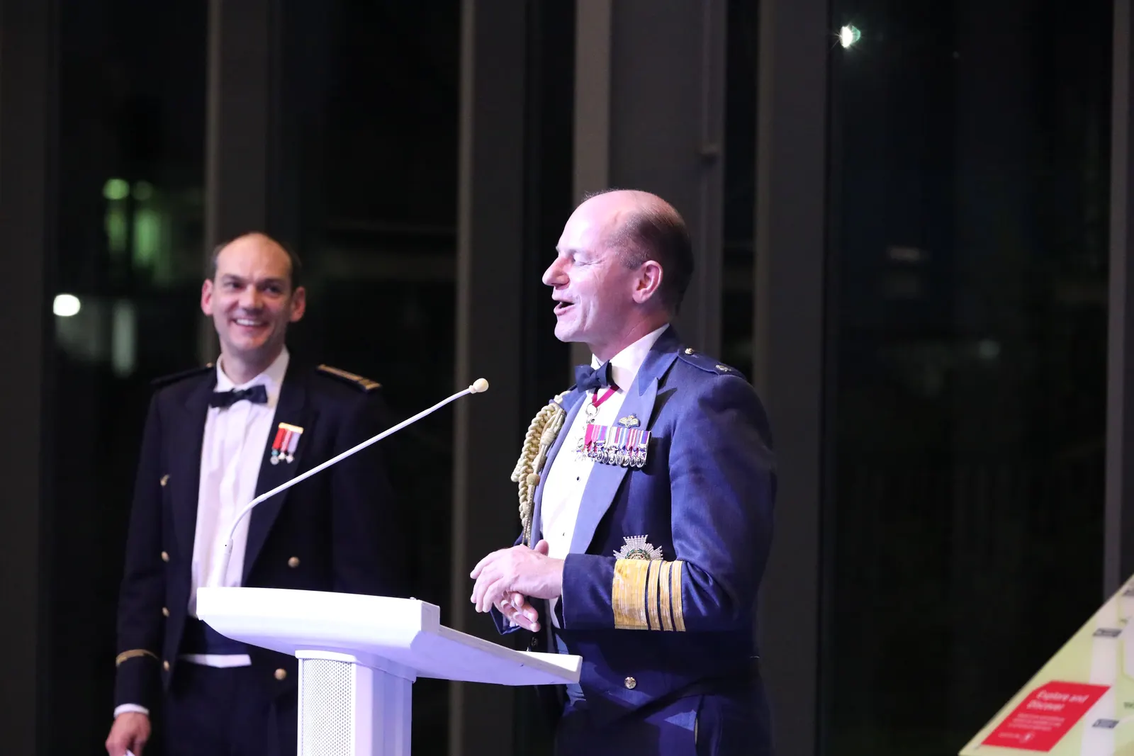 Two speakers sharing a joke during the after-dinner speeches at a black-tie gala