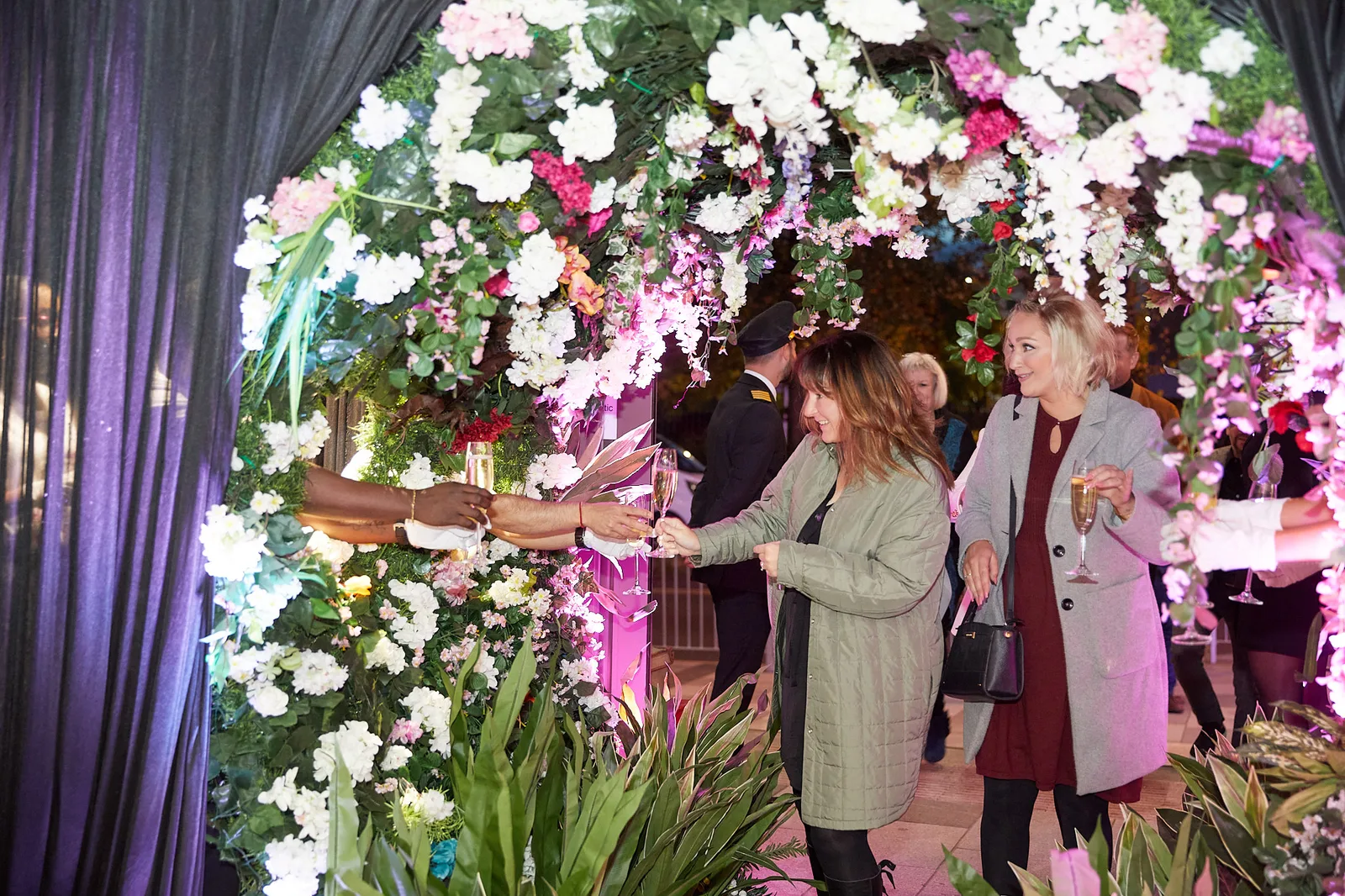 Guests welcomed with champagne through a floral arch at a themed conference reception