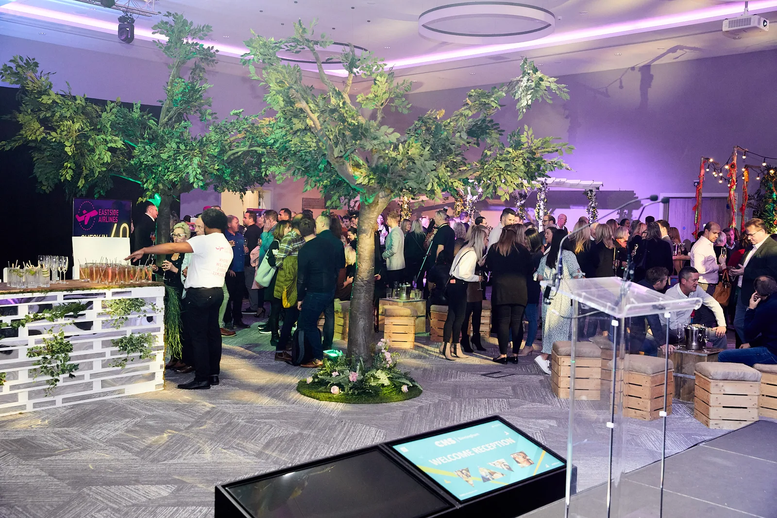 Packed welcome reception at The Eastside Rooms Birmingham with indoor oak trees and themed bar
