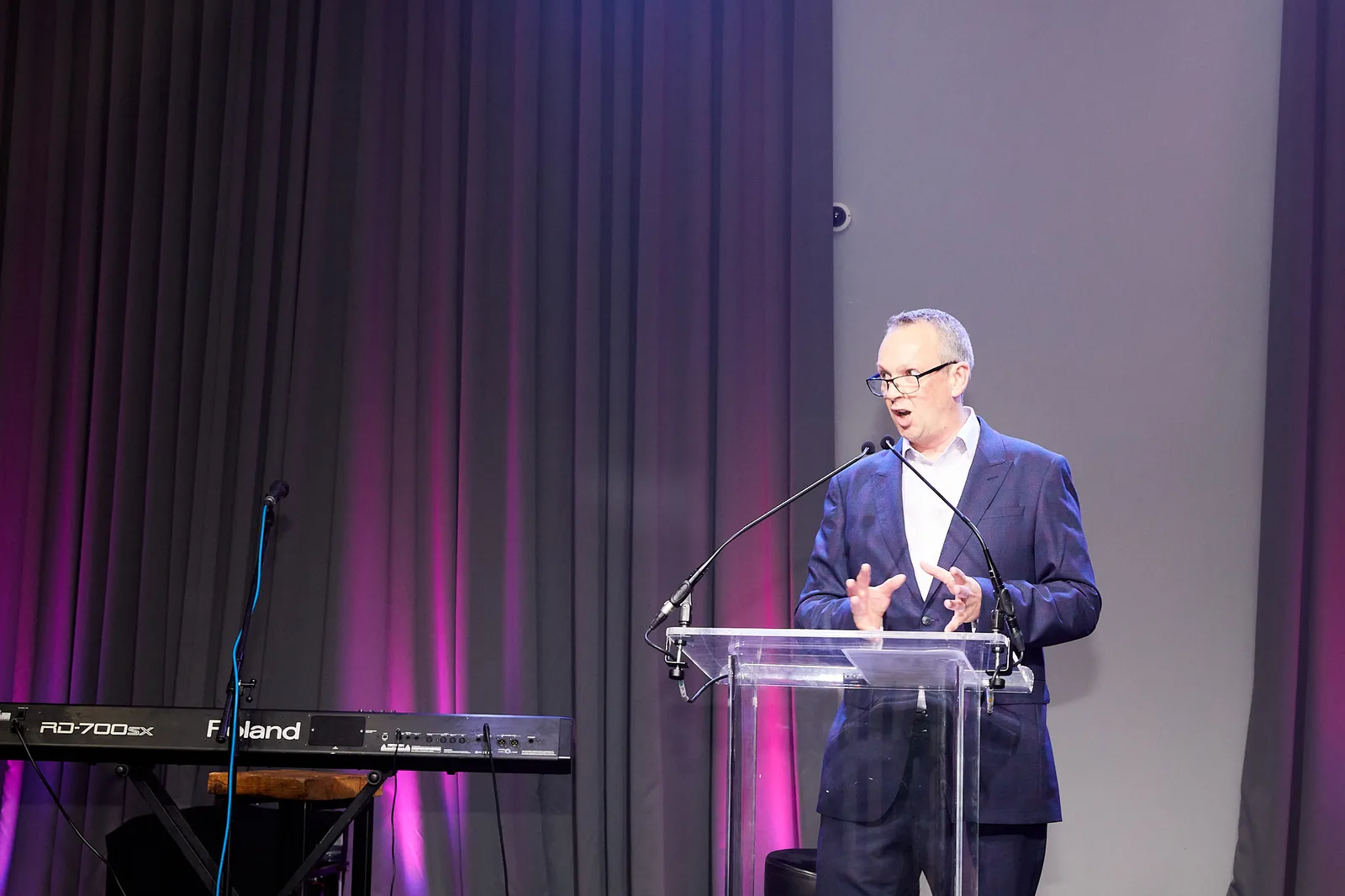 Speaker at an acrylic lectern under purple stage lighting at a Birmingham conference