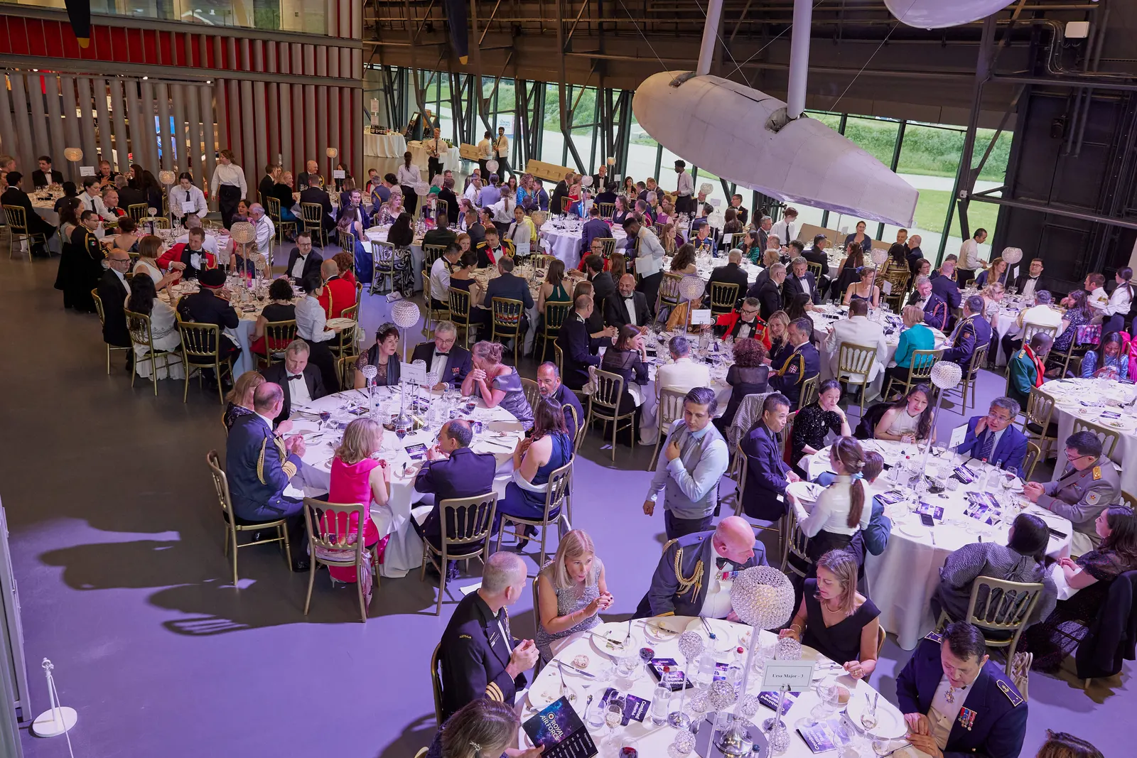 Black-tie gala dinner beneath aircraft at a museum hangar venue