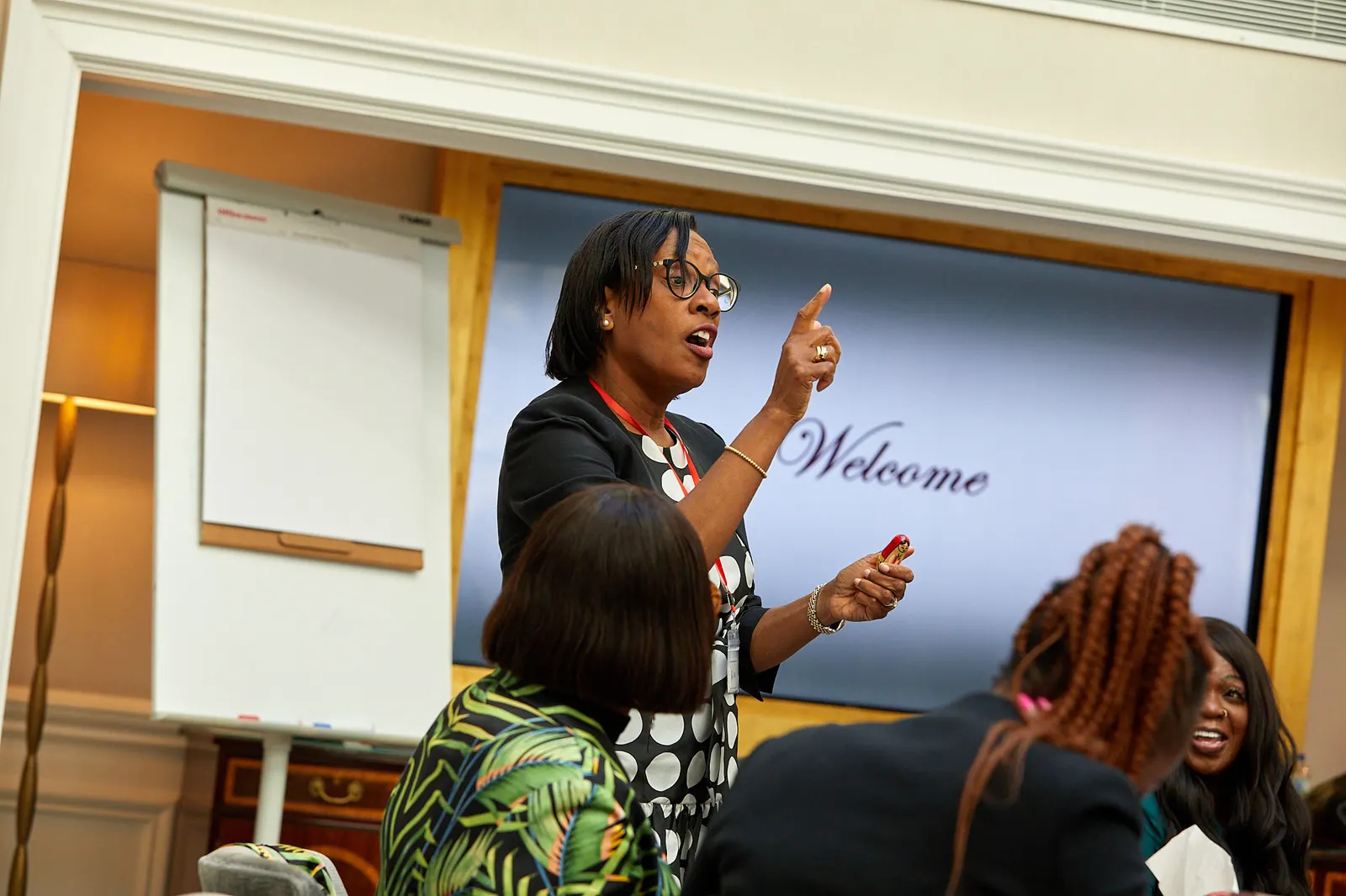 Facilitator addressing delegates at a corporate workshop, with a welcome screen behind her